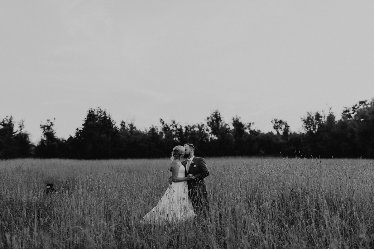 Black and white portrait of couple kissing in wheat field on their wedding day