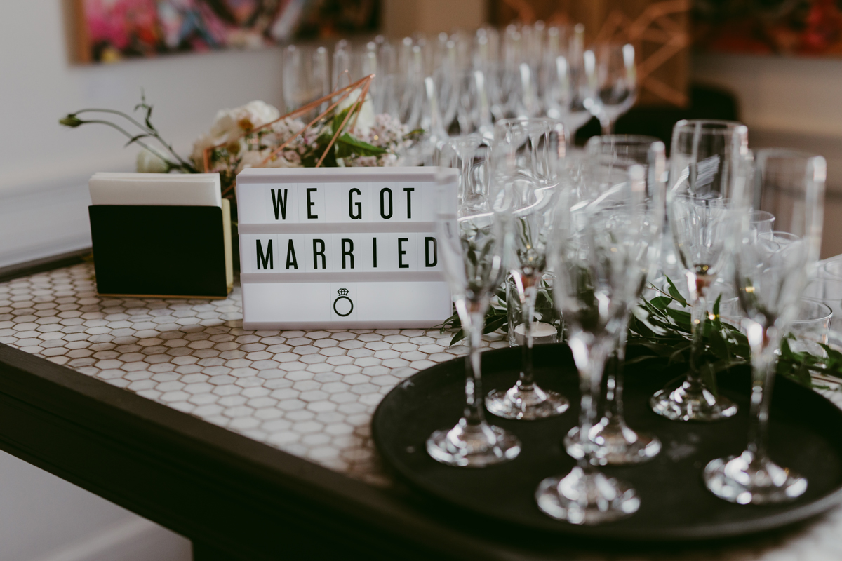 A light board that reads "we got married" on a bar alongside champagne glasses