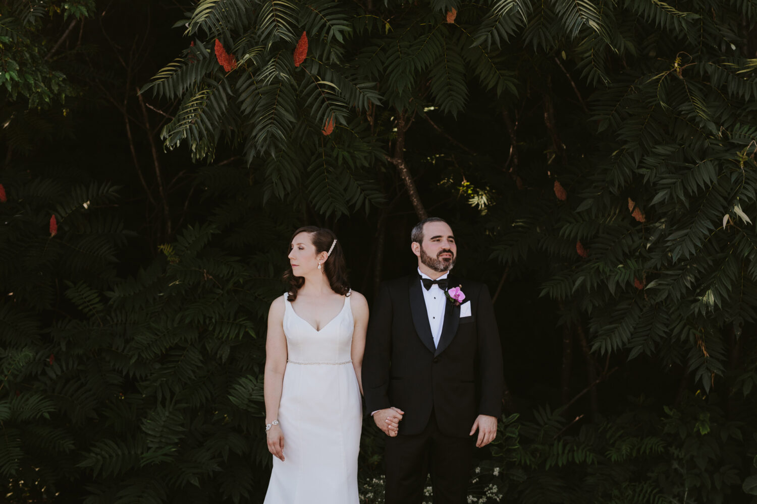 Formal portrait of bride and groom standing under tropical plants